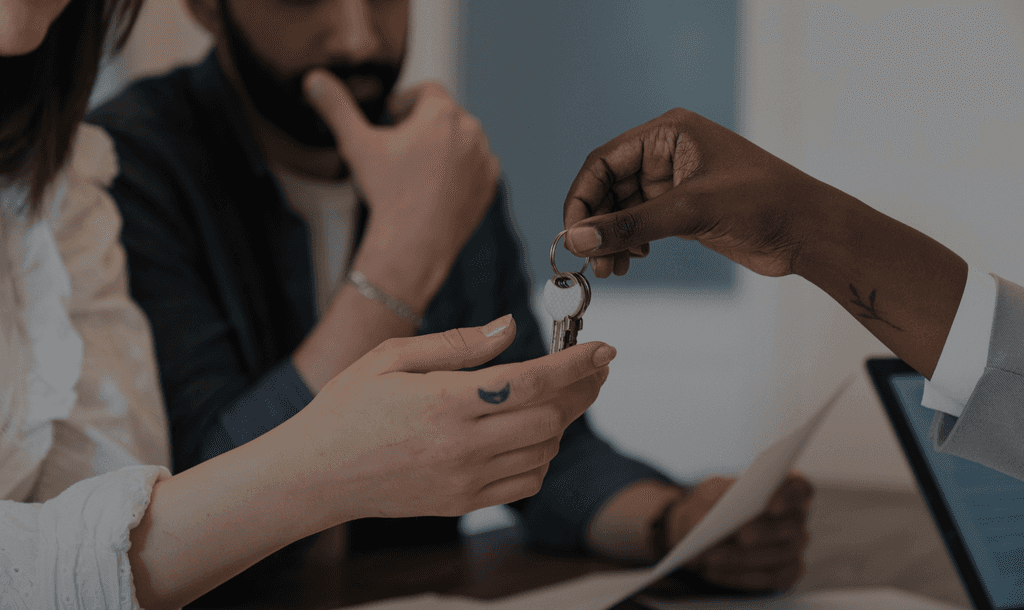 A real estate agent handing keys to a couple at a desk