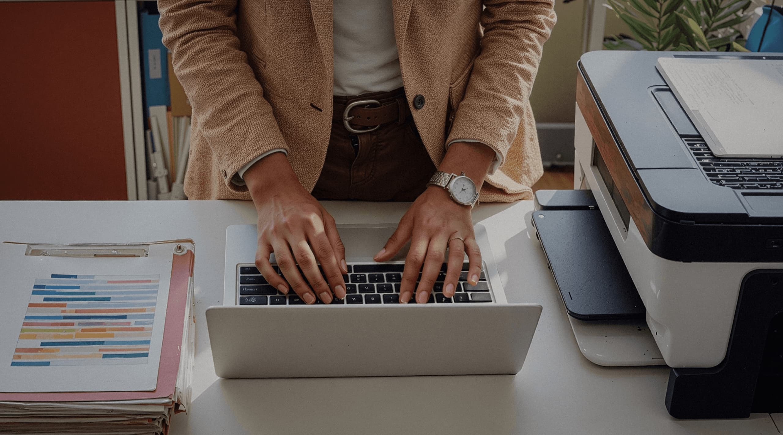 A person standing at a desk while typing on a laptop.
